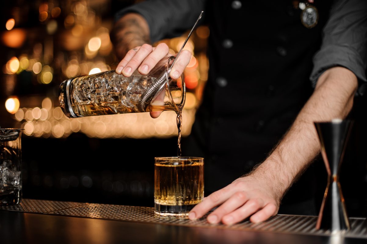 A cocktail being poured on a bar.