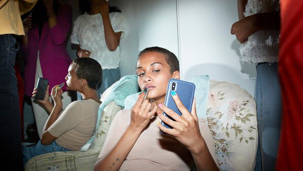 Young woman applying lipstick while looking in smart phone against mirror at home