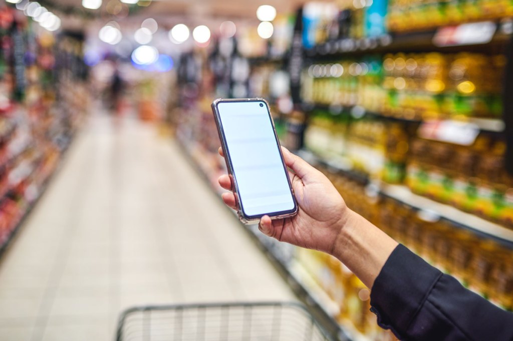 Woman holding cell phone in front of her with shopping cart in grocery food aisle